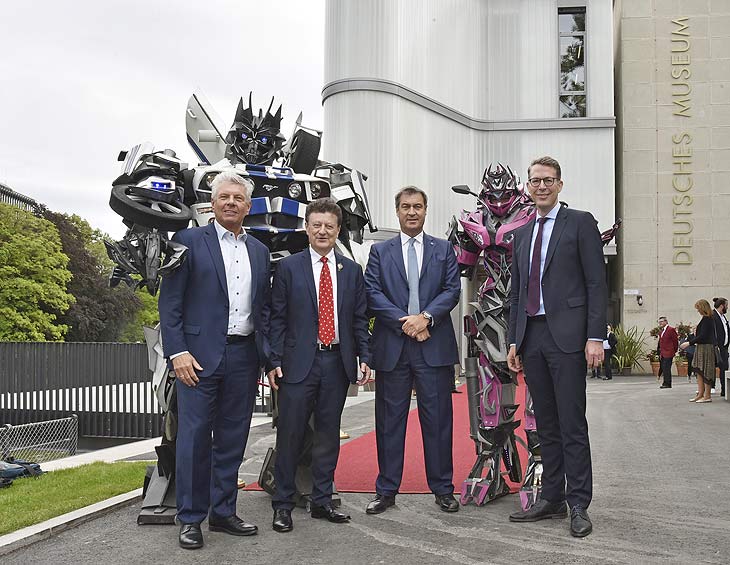 Roter Teppich vor dem neuen Eingangsgebäude des Deutschen Museums: Die Ehrengäste Münchens Oberbürgermeister Dieter Reiter (li.), Bayerns Ministerpräsident Markus Söder (2. v. re.) und Bayerns Staatsminister für Wissenschaft und Kunst Markus Blume (re.) wurden von Generaldirektor Wolfgang M. Heckl (2. v. li.) und den Transformers (im Hintergrund) begrüßt. (©foto. Deutsches Museum)